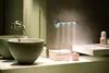 A modern bathroom sink area with a sleek faucet, two basin sinks, and a wall-mounted LED light fixture emitting a spray of water. Podgląd zdjęcia produktu
