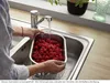 A person is washing raspberries in a sink under running water. Produktbild-Vorschau