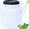 A white plastic barrel with a black lid, a pair of wooden tongs, and some cucumbers with leaves. Produktbild-Vorschau