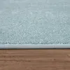 A close-up view of the edge of a light blue rug on a wooden floor. Produktbild-Vorschau