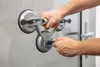 Hands using a triple suction cup lifter on a glass surface. Produktbild-Vorschau