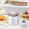 A close-up shot of a glass jar with a gray lid, placed on a white surface. Various food items, including mango slices, berries, a donut, and a bowl of yogurt, are artfully arranged around the jar. Produktbild-Vorschau