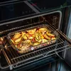 A glass baking dish filled with roasted potatoes, vegetables, and herbs is placed inside an open oven. Podgląd zdjęcia produktu