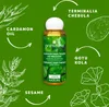 A product shot of a hair oil bottle surrounded by illustrations of herbs and text labels. Produktbild-Vorschau