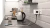 A kitchen counter with a kettle, mug, and a smartphone charging via a power strip. Náhled obrázku produktu