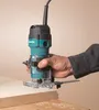 A hand holding a Makita trim router over a piece of wood. Podgląd zdjęcia produktu