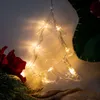 A clear LED Christmas tree decoration hanging on a wall, with some greenery and a red flower in the foreground. Produktbild-Vorschau