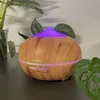 A humidifier with a wood-grain finish is shown on a dark surface, with plants in the background and a purple light emanating from the top. Náhled obrázku produktu