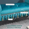 A close-up of a teal upholstered bench with decorative tassels and tufted detailing, set against a grey carpeted floor. Produktbild-Vorschau