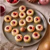 A plate of Christmas-themed linzer cookies with jam filling, arranged on a table with festive decorations. Produktbild-Vorschau