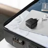 A black UGREEN 2xUSB-C 66W PD Wall Charger EU is placed on top of a silver laptop inside an open black suitcase. A passport and white wireless earbuds are also visible. Anteprima dell’immagine prodotto
