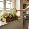 A person is arranging flowers in a wooden planter box on a windowsill. Podgląd zdjęcia produktu