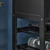 A close-up view of a black metal wine rack with bottles of wine and water on shelves, against a blue wall. Produktbild-Vorschau
