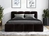 A dark brown upholstered bed with a headboard and footboard, set up in a bedroom with artwork on the wall and plants on either side. Produktbild-Vorschau