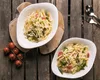 Two white pasta bowls filled with pasta, asparagus, and cherry tomatoes, placed on a rustic wooden table. Voir les images du produit