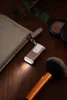 A small gold flashlight is attached to a beige makeup bag, with a makeup brush and a compact in the background. Produktbild-Vorschau