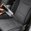A hand is using a black and orange handheld vacuum cleaner to clean a gray car seat. Produktbild-Vorschau