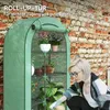 A woman is tending to plants inside a green greenhouse. Voir les images du produit