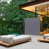 An outdoor living space with a modern sofa and a grey screen divider, surrounded by lush greenery. Anteprima dell’immagine prodotto