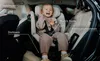 A young child is sitting in a car seat in the back seat of a car. The car seat has labels pointing out its features. Anteprima dell’immagine prodotto