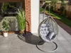 A hanging egg chair with cushions is placed on a patio next to a large window and some plants. Anteprima dell’immagine prodotto