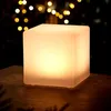 A glowing cube-shaped lamp sits on a textured surface, with blurred lights in the background. Anteprima dell’immagine prodotto