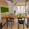 A dining room with a wooden table and chairs, set for a meal, with a moss wall feature and a modern pendant light. Náhľad obrázku produktu