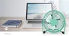 A turquoise desk fan is placed on a wooden desk in front of an open laptop displaying a beach scene. A notebook and pens are also on the desk. Podgląd zdjęcia produktu
