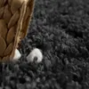 A close-up view of a shaggy rug with a woven basket and some white objects spilling out. Produktbild-Vorschau