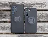 Two black smartphone cases with Quad Lock mounts are shown on a wooden surface. Produktbild-Vorschau