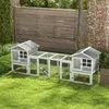 A wooden rabbit hutch with an outdoor run is set up on a grassy lawn in a backyard, with a wooden fence and brick wall in the background. Produktbild-Vorschau