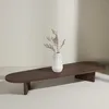 A dark brown, oval-shaped coffee table with a white vase containing dried flowers on top, set against a light gray and white background. Produktbild-Vorschau