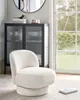 A cream-colored bouclé armchair is placed in a room with a dark cabinet and a large window overlooking greenery. Podgląd zdjęcia produktu
