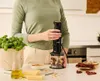 A person is using a black immersion blender in a kitchen setting, with ingredients like basil, pine nuts, cheese, and sun-dried tomatoes on the counter. Anteprima dell’immagine prodotto
