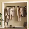 A closet with clothes hanging on two industrial-style pipe clothing racks mounted on the wall. Shoes and a tote bag are on the floor. Produktbild-Vorschau
