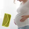 A pregnant woman is holding a small yellow-green pouch against her belly. Produktbild-Vorschau