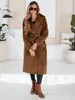 A woman wearing a brown winter coat and boots, standing in a studio setting with plants. Náhled obrázku produktu