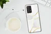 A smartphone case with an abstract pattern of gold lines on a white background, placed on a white surface next to a cup of coffee and earphones. Produktbild-Vorschau