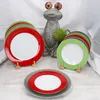 A set of colorful plates are displayed on a table with a decorative frog statue in the background. Produktbild-Vorschau