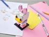 A LEGO BrickHeadz Daisy Duck figure is shown on a desk with drawing supplies. Produktbild-Vorschau