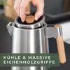 A hand is shown placing a wooden cap on a stainless steel kettle. Produktbild-Vorschau