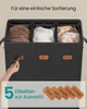 A hand is shown attaching a label to a multi-compartment laundry basket. The basket is filled with folded laundry. Produktbild-Vorschau