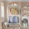 A laundry room with a rolling garment rack filled with clothes, a washing machine, and shelving. Voir les images du produit