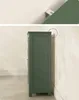 Side view of a tall, slender, dark green cabinet against a light beige wall. Náhled obrázku produktu