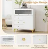 A white cabinet with a fluted glass door and gold accents, shown in a room setting with a chair and a stool. Below the main image are close-up shots of the cabinet's features. Produktbild-Vorschau