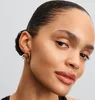 Close-up of a woman's ear wearing gold heart-shaped earrings. Anteprima dell’immagine prodotto