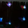 Several illuminated butterfly-shaped lights are attached to a dark, textured background, possibly a fence or screen. Produktbild-Vorschau