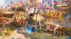 A Lego-themed scene from the game Lego Horizon Adventures, featuring a village with a food truck and a customizable building. Produktbild-Vorschau