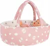 A baby doll is lying in a pink bassinet with a handle. The bassinet has a pattern of white polka dots, hearts, and teddy bears. Produktbild-Vorschau