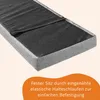 A close-up view of a grey upholstered product, possibly a bench or mattress topper, with a black fabric underside and elastic straps visible. An orange overlay with German text is at the bottom. Anteprima dell’immagine prodotto